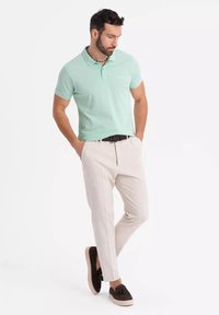 Polo shirt verde menta chiaro con collo a polo, abbinato a pantaloni beige e mocassini neri con un design sottile.