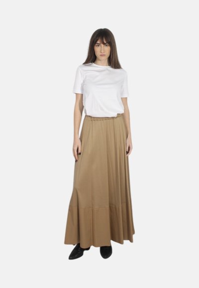 Top bianco a maniche corte abbinato a una gonna maxi beige con una vita arricciata e un sottile design a strati. Footwear nero completa il look.