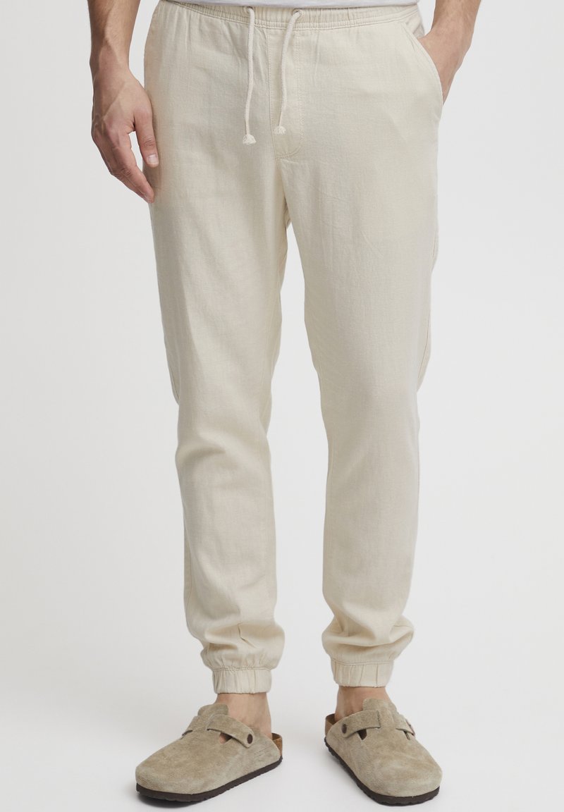 Joggers de lino color beige claro con cintura elástica y cordón. Presentan puños elásticos y bolsillos laterales. Se llevan con zuecos de ante beige.