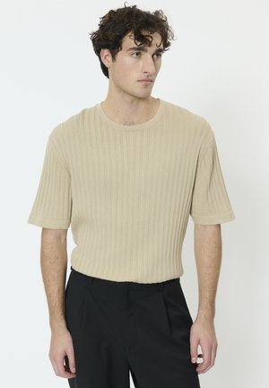 Maglione beige a maniche corte con costine, scollo rotondo e texture morbida, abbinato a pantaloni neri. Design semplice e moderno.