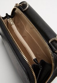 Sorte tekstureret faux læder crossover taske med guldfarvet hardware, med en lynlåscompartiment og en beige stofforing. Bemærkelsesværdige logodetaljer indeni.