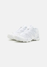 Pantofi sport albi cu un superior din plasă texturată, talpă din cauciuc și un design distinctiv în valuri pe laterale. Dispune de închidere cu șireturi.