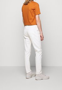 Jeans blancos con bolsillos traseros combinados con una camiseta de mangas cortas naranja y zapatillas de deporte gris claro. Diseño simple, ajuste casual y colores sólidos.