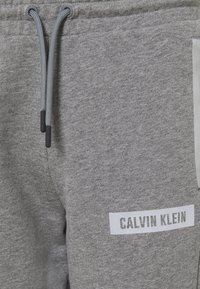 Grijze katoenen joggingbroek met een elastische tailleband met een trekkoord, zijzakken en een witte logopatch met "CALVIN KLEIN" erop gedrukt.