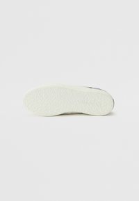 Hvit sneakersåle med teksturert, gummiert overflate. Rund form, flat design og minimal merkevarevisning.