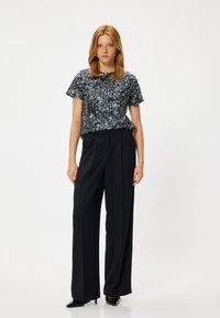 Korte mouwen top met een bloemenpaillettenpatroon in donkerblauw, gecombineerd met zwarte wijde broek. Glanzende zwarte hakken maken de outfit compleet.