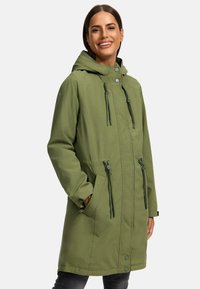 Olijfgroene parka jas met capuchon, trekkoorden in de taille en drukknoopsluitingen. Heeft zijzakken en een gladde, iets reflecterende textuur.