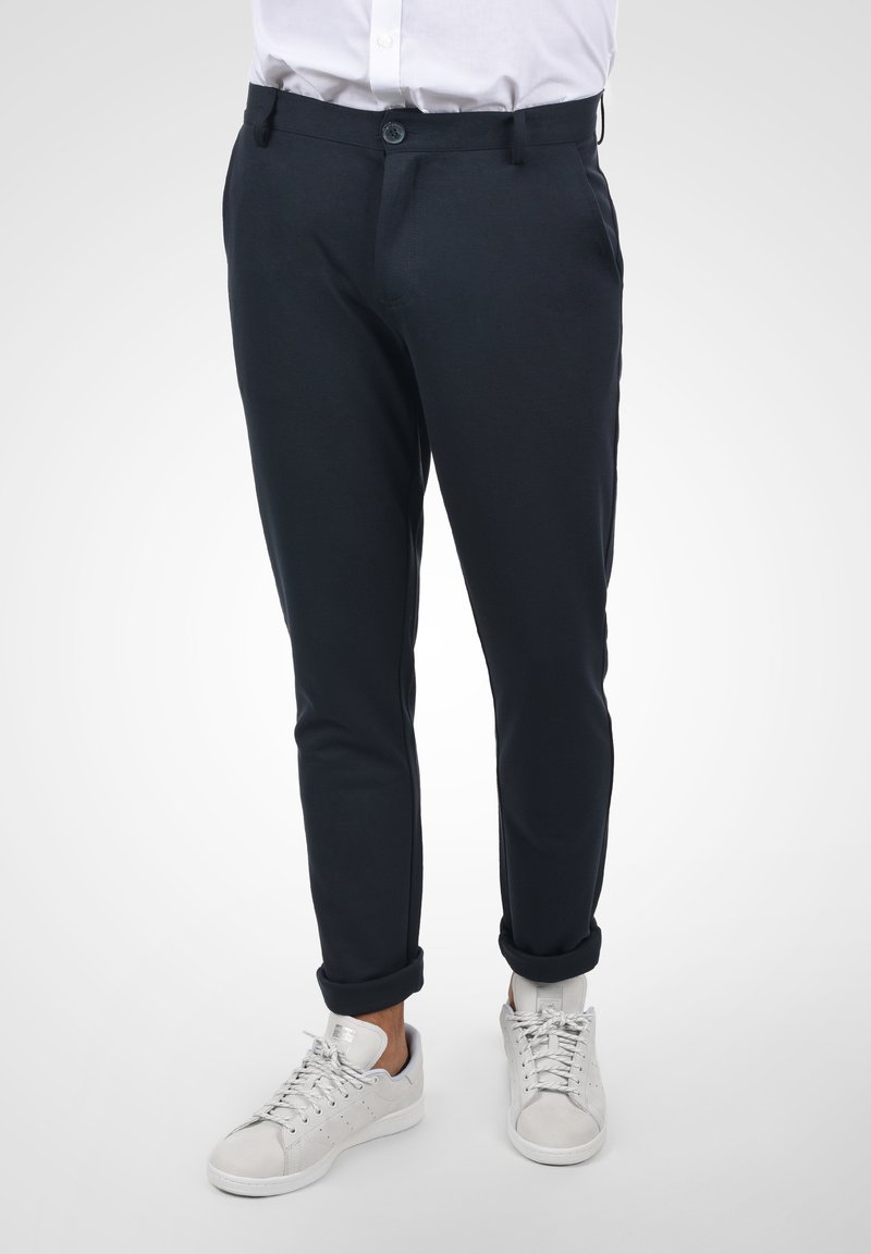 Marineblå chinos med slim fit, glat overflade, frontlommer og enkelt knaplukning, parret med hvide sneakers.