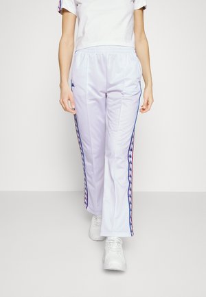 Białe sportowe spodnie z niebieskimi bocznymi paskami z powtarzającym się wzorem logo, elastyczną talią oraz pasujące sportowe buty.