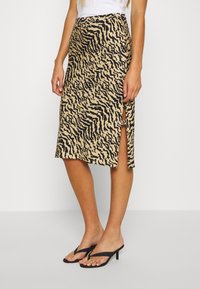 Beige kjol med svart zebramönster, midiklängd, med en sidoklyfta. Pairad med svarta flip-flops. Slät tygtextur.