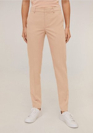 Beige tailored pants worn with white sneakers, shown from waist to feet against a plain background.