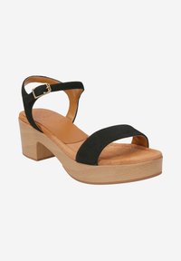 Black suede sandal with two wide straps, adjustable ankle buckle, and a light wood block heel. Leather insole with a soft texture.