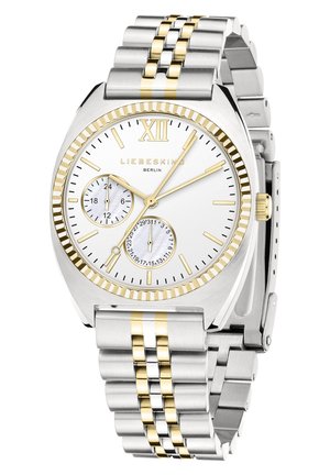 Reloj de pulsera plateado y dorado con esfera blanca, número romano doce, dos subesferas, marcadores dorados y una pulsera de eslabones metálicos.