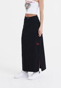 Sort maxiskirt med sideslids og lommer i lappen, parret med en hvid crop top og hvide sneakers. Fremstillet af et glat og holdbart stof.