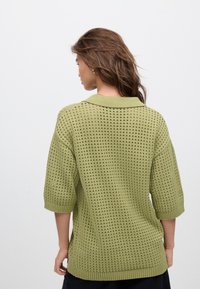 Maglione verde lavorato a maglia caratterizzato da una vestibilità ampia, maniche a mezzo braccio, colletto e motivo a buchi aperti, con bordi a costine sui polsini e sull'orlo.