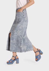 Gonna di jeans con spacco laterale, caratterizzata da una tonalità blu chiaro e un motivo testurizzato. Abbinata a sandali blu con tacco a blocco intrecciato.