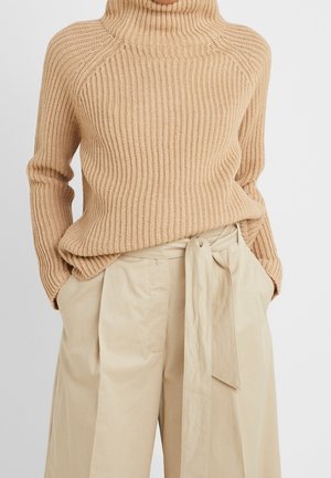 Pull col roulé côtelé beige assorti à un pantalon beige taille haute à jambes larges, avec ceinture en tissu nouée et poches.