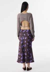 Pull en tricot gris avec un dos ouvert, associé à une longue jupe fluide fleurie violette, avec une base marron foncé et une texture douce.