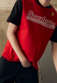 Camiseta de manga corta en rojo y negro con el logo de "Scuderia Ferrari". Hecha de algodón, con textura suave y corte cómodo.