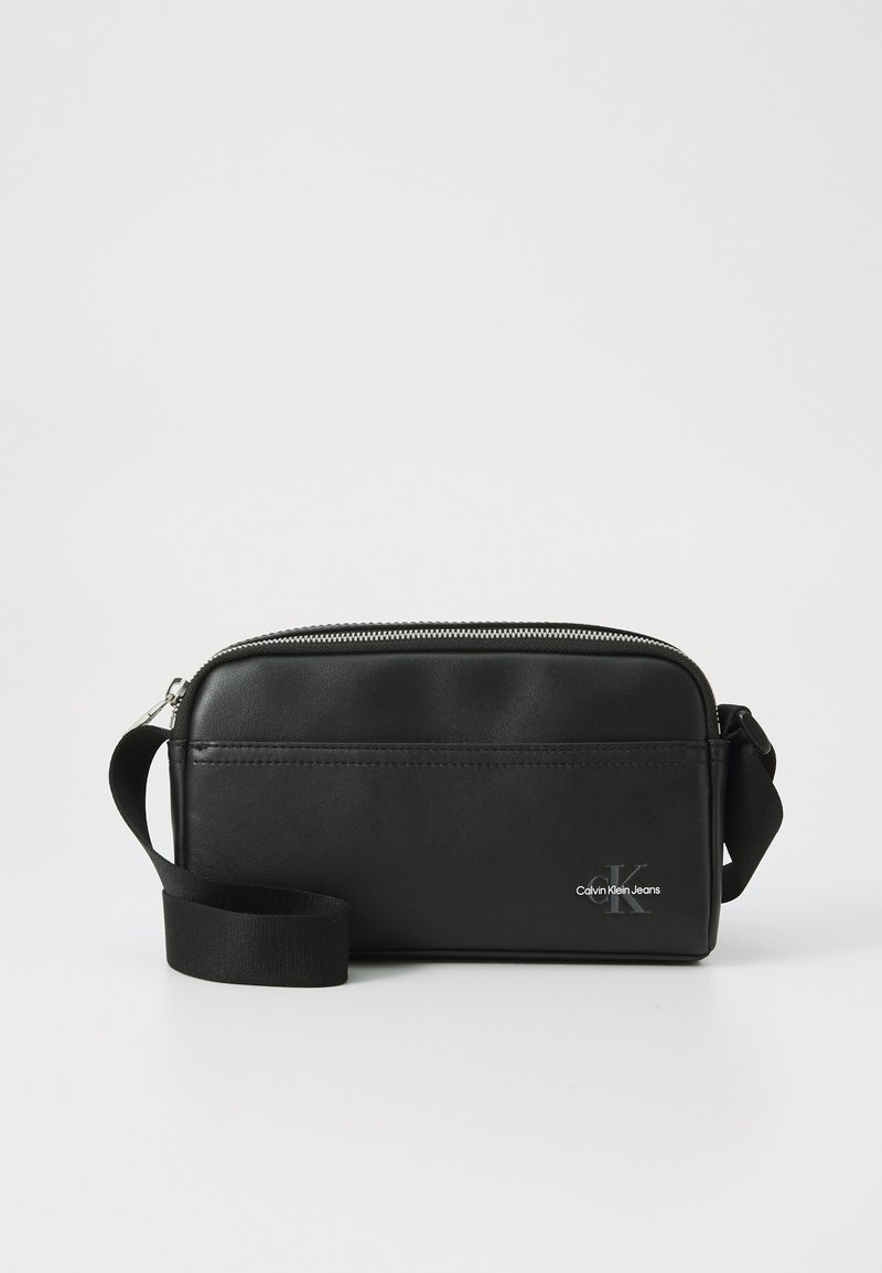 Bolsa de couro preto com fecho de zíper, formato retangular, alça ajustável e um destacado logótipo da Calvin Klein Jeans na frente.
