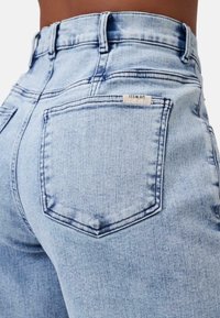 Jeans in denim blu chiaro con vita alta, due tasche posteriori e aree leggermente sbiadite, con un'etichetta piccola vicino alla vita.