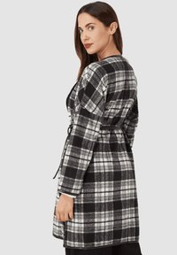 Cárdigan de cuadros en blanco y negro con cintura ceñida, mangas largas y una textura suave, que presenta patrones a cuadros y un corte relajado.