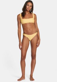 Completo bikini a quadretti giallo e rosa con top a scollo quadrato e slip a vita bassa. Il materiale sembra liscio con un design aderente.