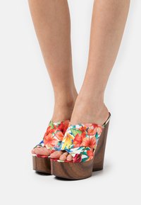 Bloem motief platform mules met een levendig patroon van rode en gele bloemen, open teen en een gestructureerde houten wiggenhak.