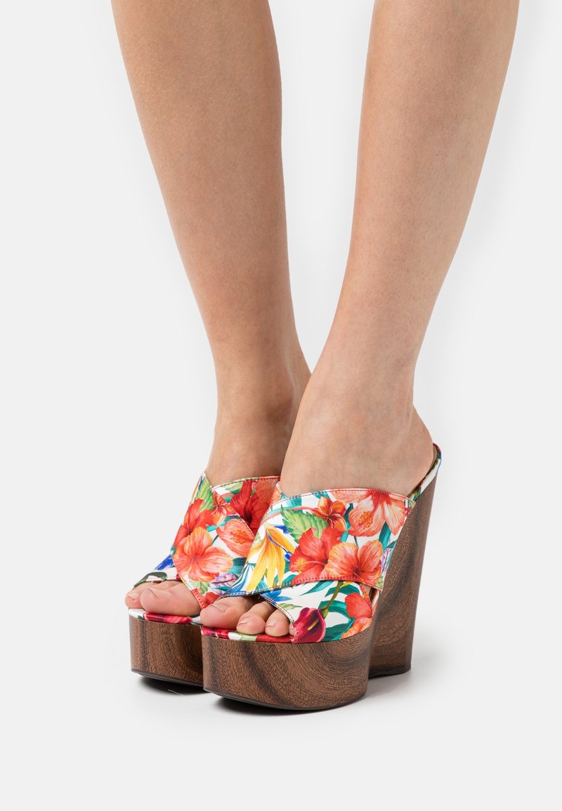 Bloem motief platform mules met een levendig patroon van rode en gele bloemen, open teen en een gestructureerde houten wiggenhak.