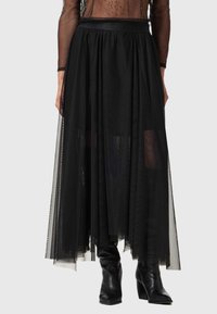 Jupe maxi en tulle noir au design fluide, dotée d'une taille ajustée et de couches de tissu semi-transparent. Associée à des bottes noires montantes.