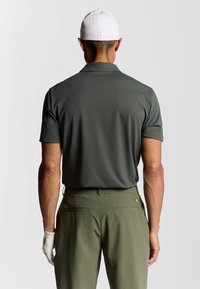 Polo shirt corto grigio scuro, in tessuto liscio, abbinato a pantaloni verdi chiari con tasche posteriori e piccolo dettaglio del logo giallo.