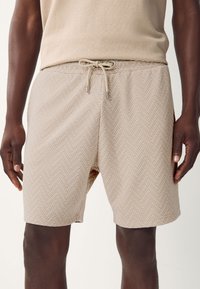 Bézs színű fürdőnadrág texturált halszálka mintával, állítható húzózsinóros derékkal és oldalzsebekkel. Sima anyagból.