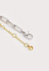 Bracciale in catena argento e oro con anelli misti; presenta un charm a forma di cuore e una chiusura a moschettone.