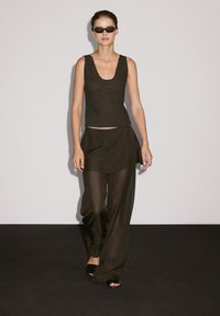 Débardeur noir en tricot avec un col en scoop, associé à une jupe ample et transparente noire sur un pantalon large et des chaussures noires à bout ouvert.