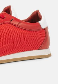 Sneaker rossa con tomaia in rete testurizzata, accenti in pelle liscia e controcanto bianco. Suola in gomma con motivo di battistrada marrone chiaro.