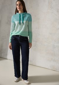Lichtgroen en teal gestreepte hoodie met verstelbare trekkoorden, gecombineerd met donkerblauwe straight-leg jeans en witte sneakers.