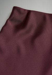 Gładki, ciemny burgundowy materiał z delikatnymi fałdami i miękką teksturą, ułożony na jednolitym jasnym tle.