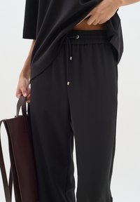 Černé, lehké, volné kalhoty s elastickým pasem a šňůrkou. V kombinaci s tmavým oversized topem a hnědou taškou.