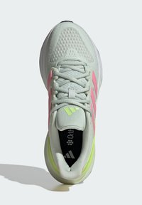 Zapatilla deportiva verde claro con una parte superior texturizada, que presenta acentos en rosa y amarillo, una suela acolchada y detalles reflectantes. Los cordones son grises.