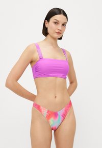 Μωβ μπικίνι τοπ με φαρδιές τιράντες, διακοσμημένο με λεπτομέρεια λογότυπου. Το κάτω μέρος έχει πολύχρωμο tie-dye σε ροζ, μπλε και πορτοκαλί αποχρώσεις, με λεία υφή.