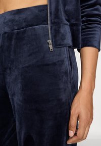 Marineblaues Samtoberteil mit Reißverschluss und verkürztem Design, das eine glatte Textur und kontrastierende Reißverschlussbeschläge aufweist, kombiniert mit passenden Hosen.