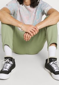 T-shirt gris clair et pastel à motifs tourbillonnants, associée à un pantalon de survêtement vert. Baskets noir et blanc avec un design à lacets. Coupe confortable et décontractée.