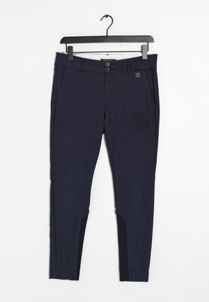 Marineblå slanke bukser med dobbelt knap- og lynlåslukning, sidelommer og sorte paneler på inderste nederste ben, hængende på sort bøjle.