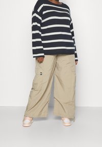 Maglione a righe blu navy e bianco a maniche lunghe abbinato a pantaloni cargo beige larghi e sneakers arancioni chiari. La texture sembra morbida e informale.
