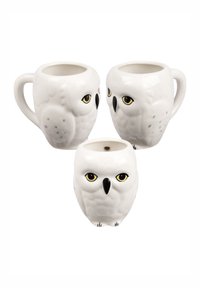 Tazze di ceramica a forma di gufo, bianche con dettagli delle piume, occhi gialli e becco nero, dotate di un manico sul lato.