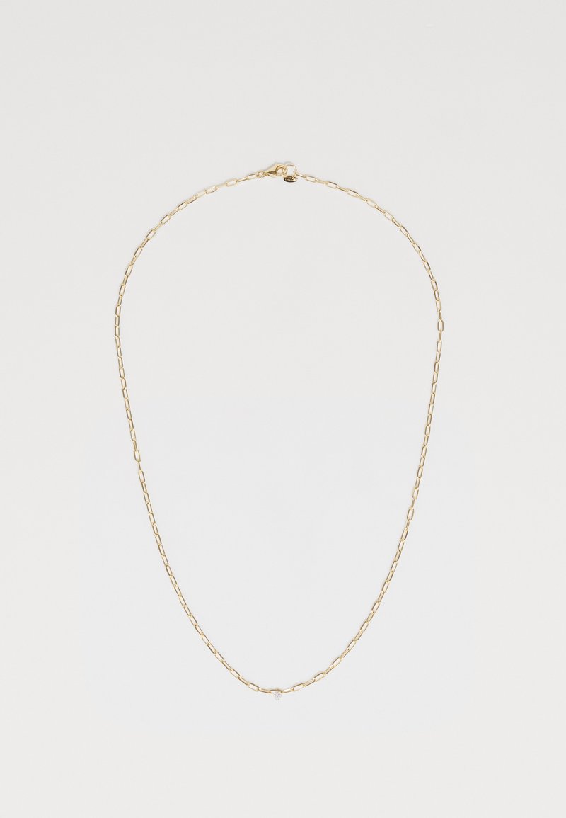 Guldkedja med avlånga länkar, med en liten diamantliknande detalj nära mitten. Slät textur, minimalistisk design.