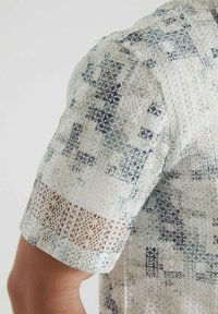 Chemise à manches courtes en tissu léger avec un motif géométrique dans des teintes de bleu et de blanc, avec des accents texturés et un ourlet en dentelle.