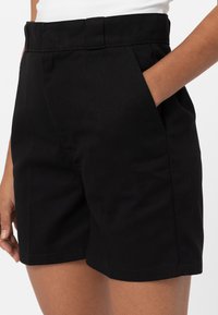 Černé kraťasy s přiléhavým střihem, vyrobené z bavlny. Mají boční kapsy, hladkou strukturu a úhledné švy podél lemu.
