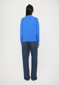 Blå strikket genser med lange ermer, rund hals og ribbestrikket kant, kombinert med løse, mørke denimjeans med baklommer og rett ben.
