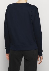 Sudadera azul marino con puños y dobladillo acanalados, diseño de cuello redondo y tejido suave y liso. Detalles de costura visibles en los hombros.